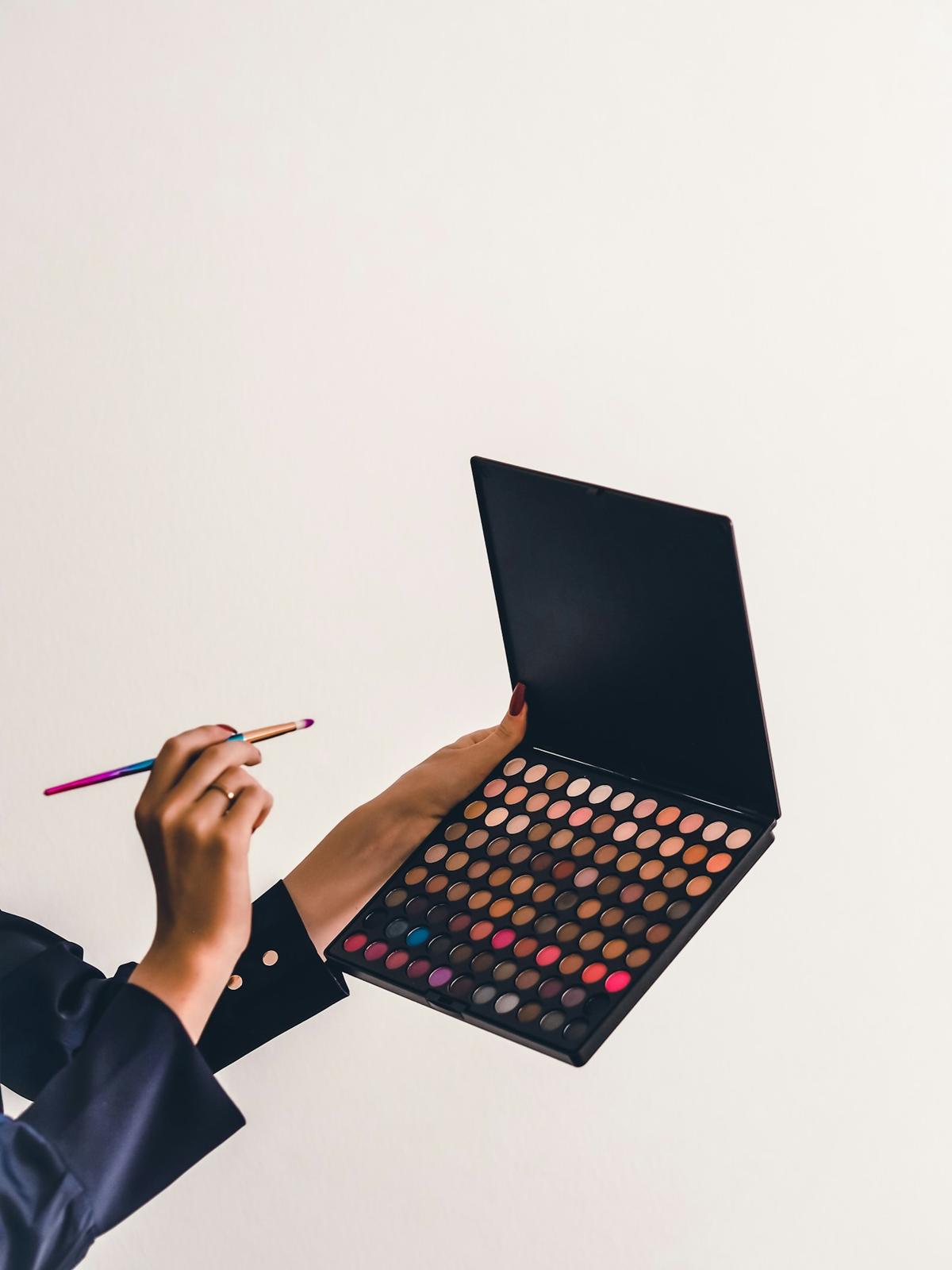 Hand holding a makeup palette and a brush