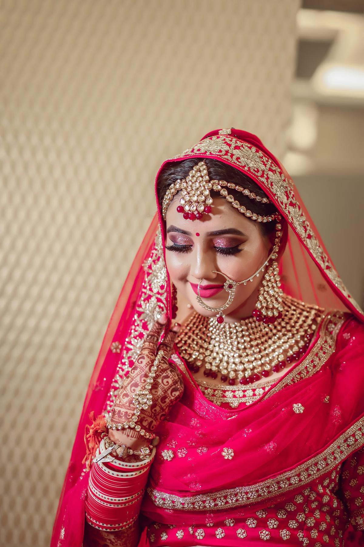 Bride in a red lehenga with gold jewellery and bridal makeup
