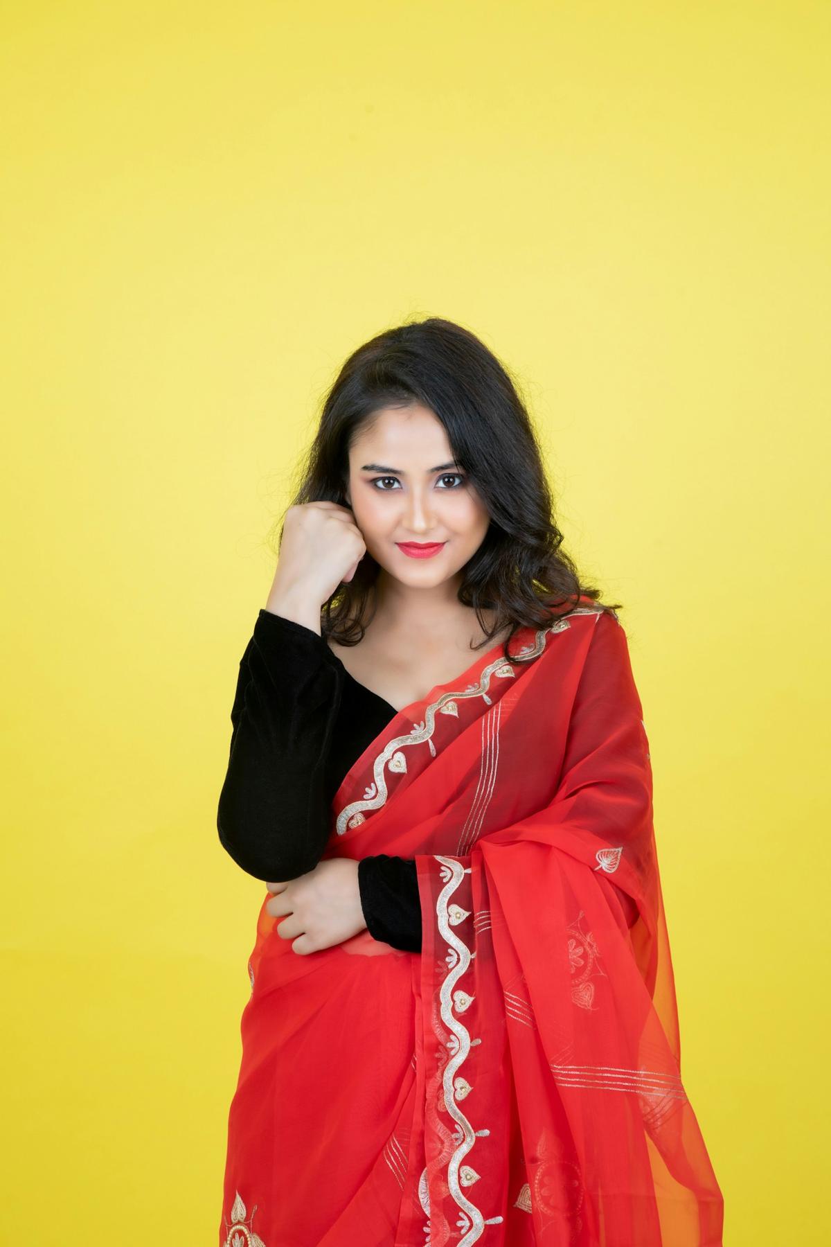 Woman in a red saree with party makeup against a yellow backdrop