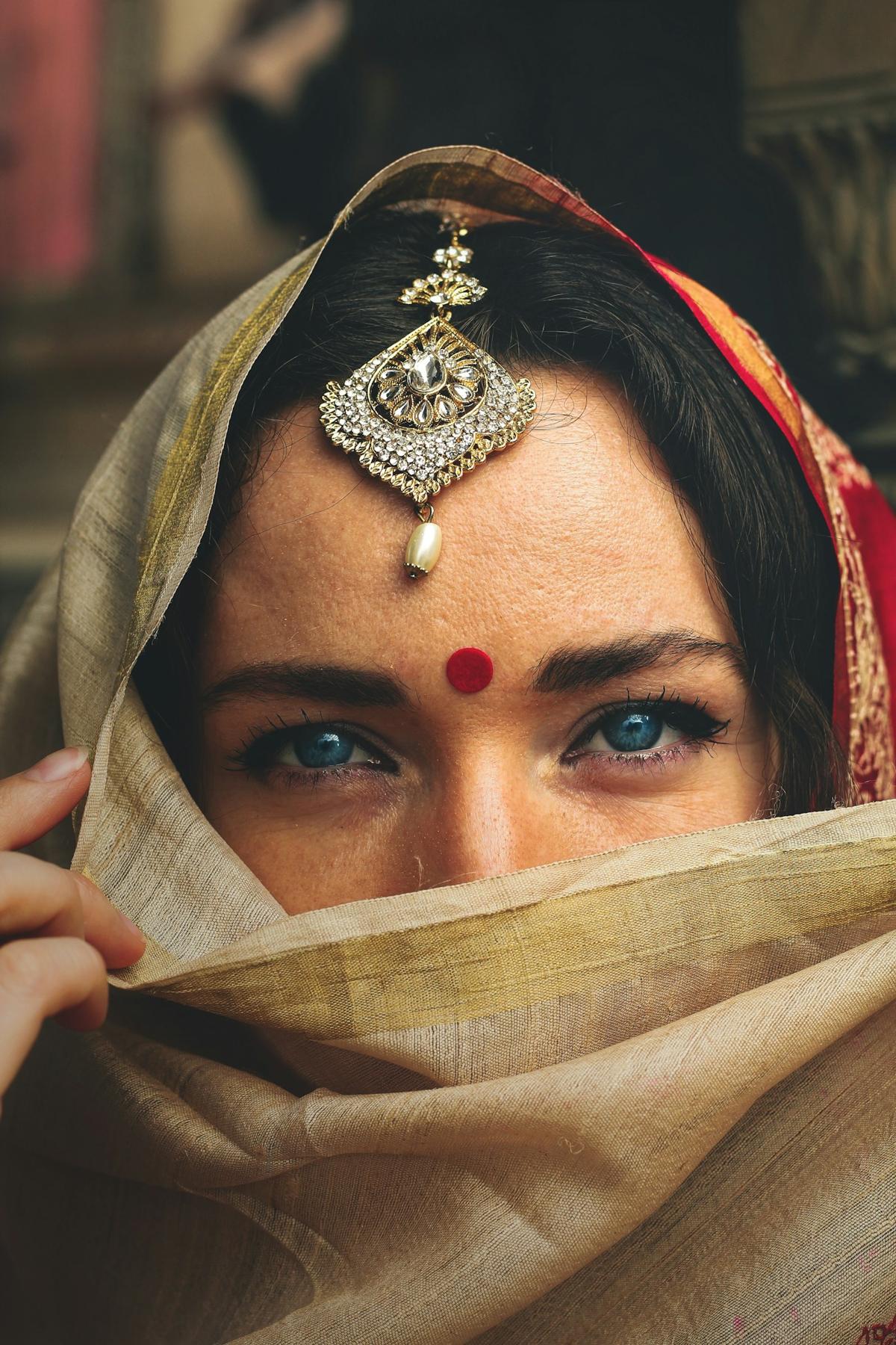 Editorial portrait of a woman with a maang tikka and veil held across her face