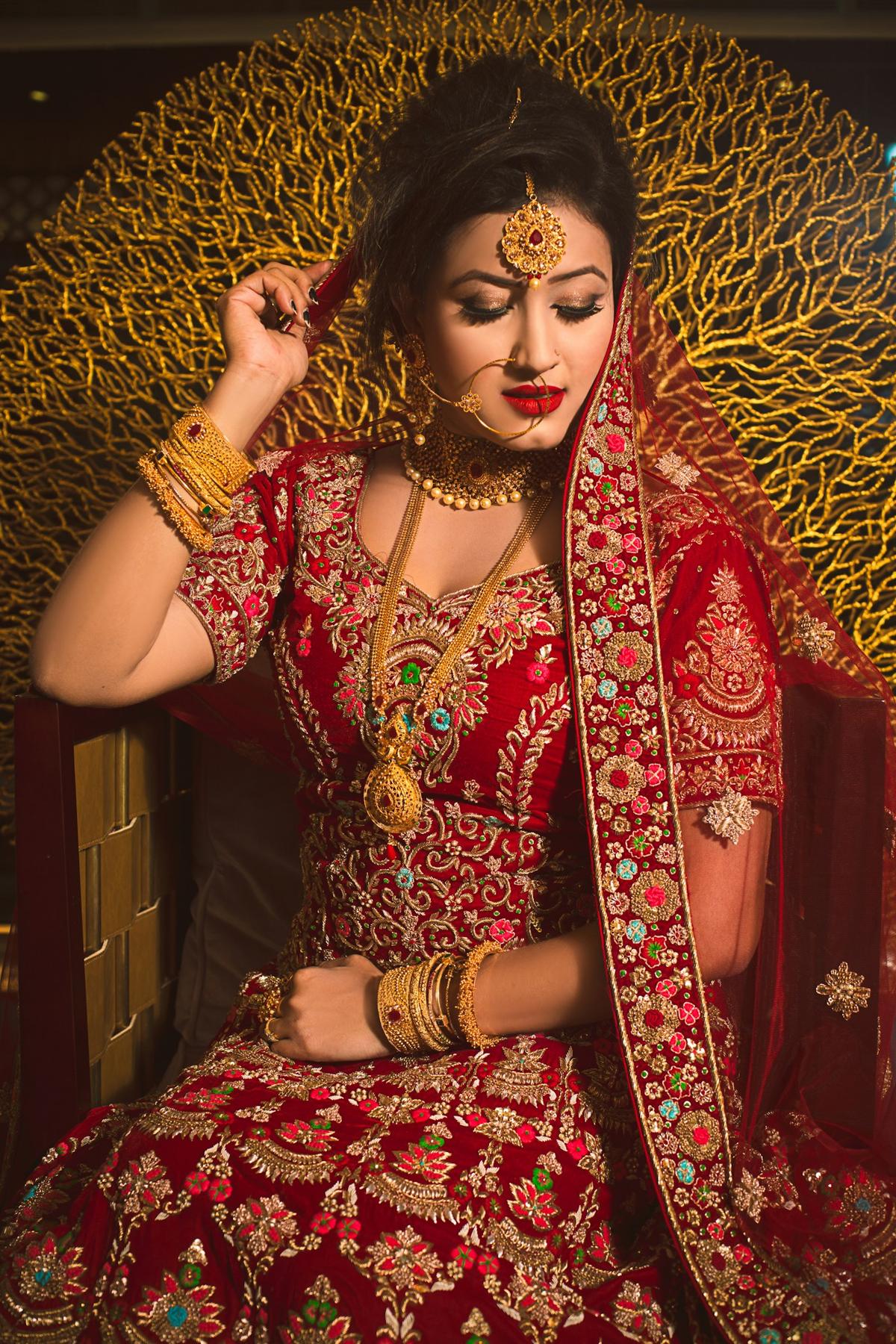 Bride in an ornate red and gold lehenga seated against a gold backdrop