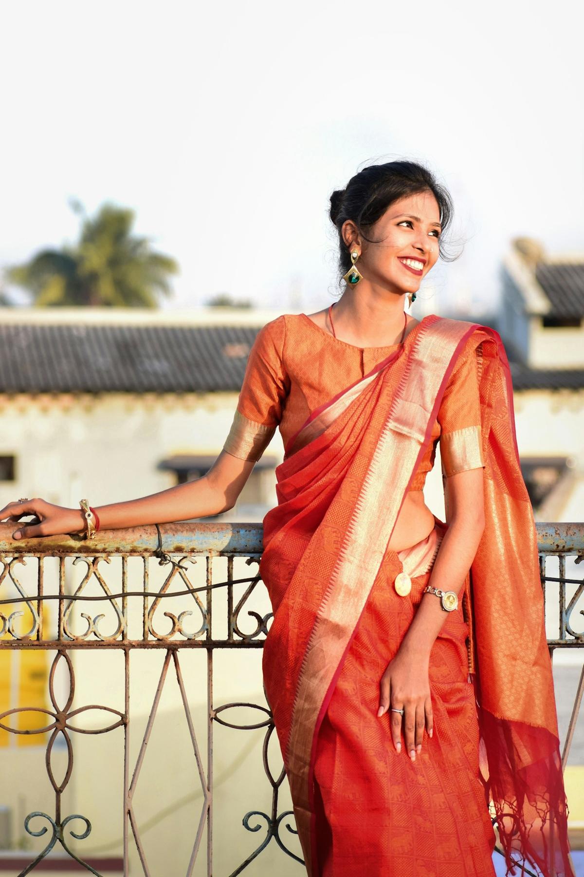Woman in an orange silk saree standing on a balcony
